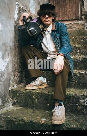 Man holding boombox on his shoulder sitting on stairs. 90s retro style nostalgia concept. Stock Photo