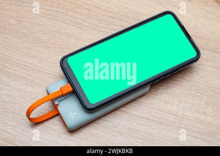 Smartphone with mockup screen, recharging from a power bank on the table, colored gadget Stock Photo