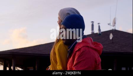 Happy multiethnic couple smiles and hugs, looks at beautiful sunset enjoying nature during vacation trip in the countryside. Young family of travelers rest after hike in the mountains. Slow motion. Stock Photo