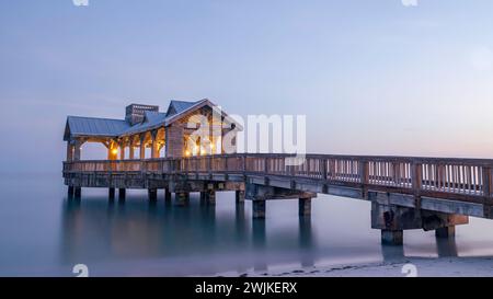 Wooden pier, located in Key West, Florida, reaching out into very calm tropical waters at sunset. There are lights on the structure Stock Photo