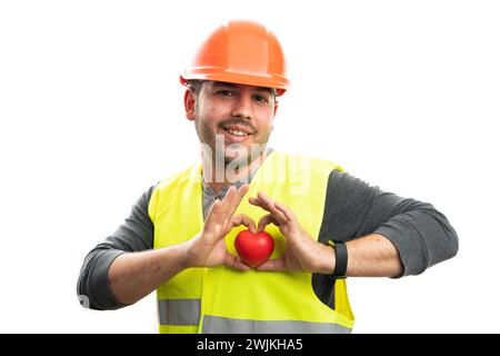 Happy builder man making cheerful friendly expression holding red heart with love gesture using fingers isolated on white background Stock Photo