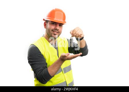 Friendly adult builder man in work clothing fluorescent vest and orange safety hardhat presenting home keys with palm isolated on white background Stock Photo