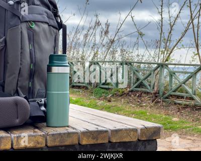 Backpack and thermos standing on wooden table in nature park Stock Photo