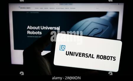 Person holding smartphone with logo of Danish cobot company Universal Robots AS in front of website. Focus on phone display. Stock Photo