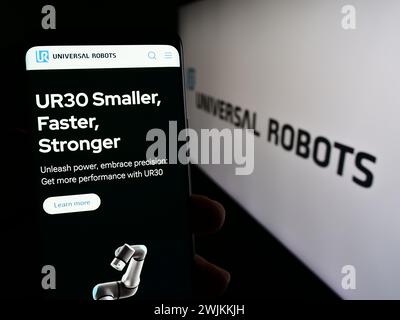 Person holding smartphone with webpage of Danish cobot company Universal Robots AS in front of logo. Focus on center of phone display. Stock Photo