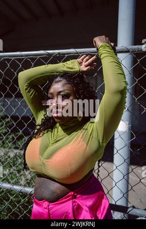 Black woman poses in front of wire fence in harsh sunlight Stock Photo