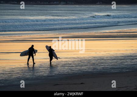 Two silhouetted surfers walking on the beach Stock Photo