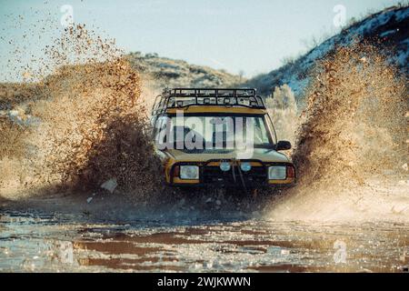 A backlit SUV drives through a puddle in the mountains. Stock Photo