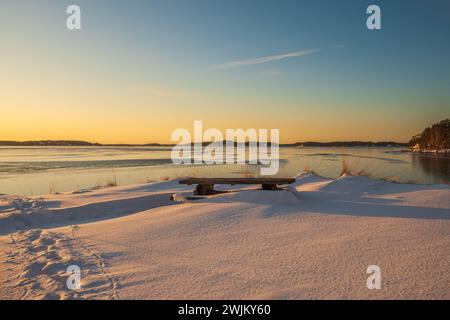 Swedish nature in Winter. Sunset over a frozen sea with a bench overlooking the water Stock Photo