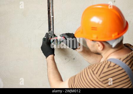 Electrician male in uniform, protective gloves and helmet checks presence of electrical voltage in socket phase uses electrical tester screwdriver.Exa Stock Photo