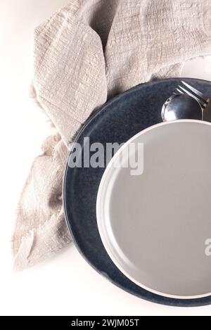 table setting with two empty ceramic gray plate with cutlery and and a napkin on white table. Neutral colors. Stock Photo