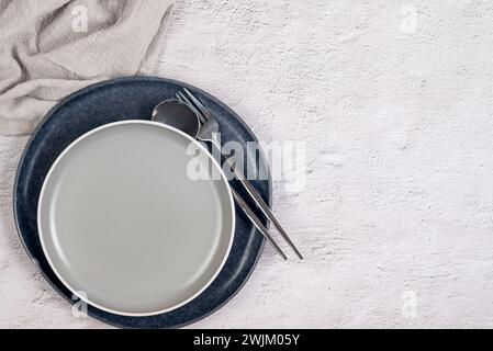table setting with two empty ceramic gray plate with cutlery and and a napkin on white table. Neutral colors. Stock Photo