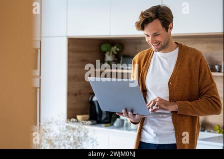 Adult man using laptop while standing in kitchen Stock Photo