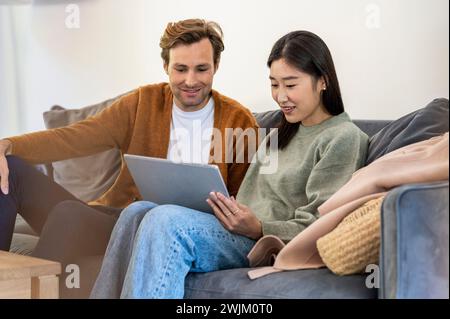 Adult couple using digital tablet while sitting on sofa Stock Photo