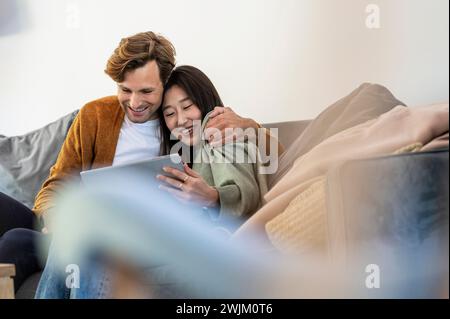 Adult couple snuggled while using digital tablet in living room Stock Photo
