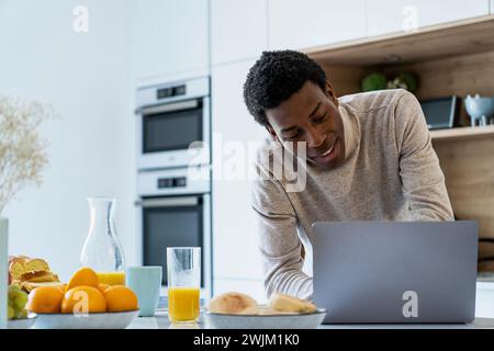Adult man using laptop while leaning on kitchen counter Stock Photo