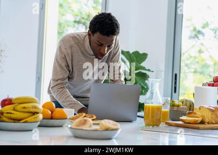 Adult man using laptop while standing at kitchen counter Stock Photo