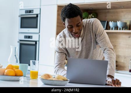 Adult man using laptop while leaning on kitchen counter Stock Photo