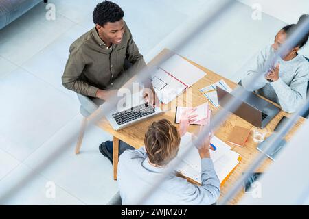 Businessmen and businesswoman discussing work while at desk using laptop Stock Photo
