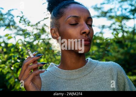 Adult woman smoking while standing outdoors with closed eyes Stock Photo