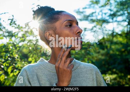 Adult woman smoking while standing outdoors during day time Stock Photo