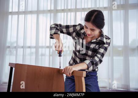 Women using screwdriver to installation screw and assembling new chair while making home furniture. Stock Photo