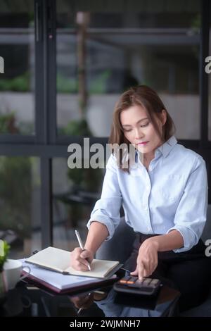 Asian businesswomen using calculator calculate financial statistics and checking marketing business document to taking notes while analyze investment Stock Photo