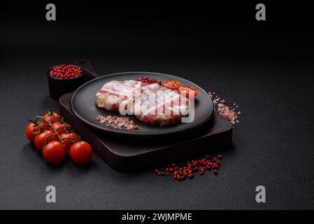 Round minced chicken or pork cutlet wrapped in bacon with salt, spices and herbs on a dark concrete background Stock Photo