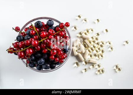 Glass bowl with ripe berries and various types of vitamin D Stock Photo