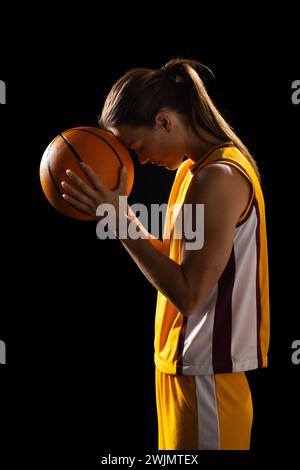 Focused young Caucasian female basketball player holds a basketball on a black background Stock Photo