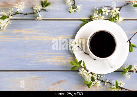 Spring composition of cup of fresh black coffee and cherry blossom branches on blue wooden background. Coffee break. Spring flowers. Flat lay, top vie Stock Photo