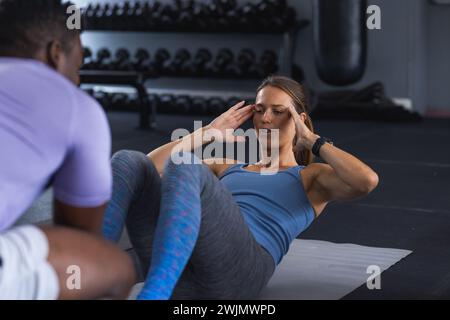 A fit African American man coaches a young fit Caucasian woman at the gym Stock Photo