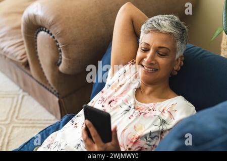 A mature biracial woman appears relaxed while using her smartphone at home, with copy space Stock Photo