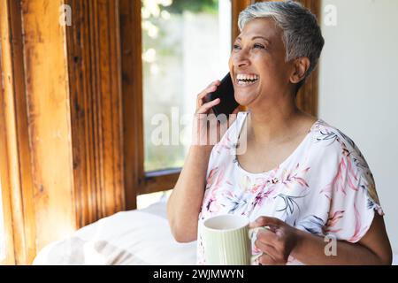 A mature biracial woman enjoys a conversation on her phone at home Stock Photo