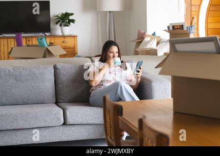 Young plus size biracial woman relaxes on a couch at home, surrounded by moving boxes Stock Photo