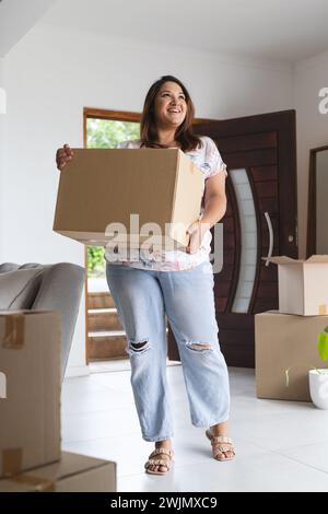 Young biracial plus size woman carries a moving box at home, with copy space Stock Photo