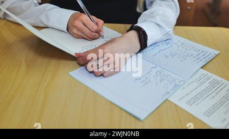 A girl student writes math formulas in a notebook. Notebook close-up. Stock Photo