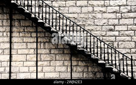 Artistic image shows black, wrought iron staircase rising diagonally on old historic stone building. Stock Photo