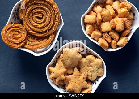 Close up photo of assorted , fresh Diwali snacks or faral items filled in white bowls with a clear black background. Stock Photo