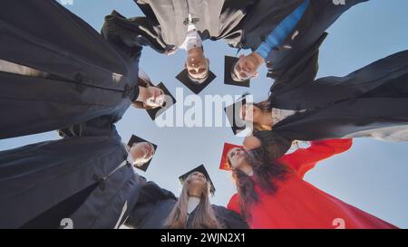 College graduates in a circle stand hugging each other. Stock Photo