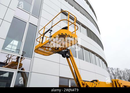 The basket of a aerial work platform is bright yellow against the background of a white building. Stock Photo