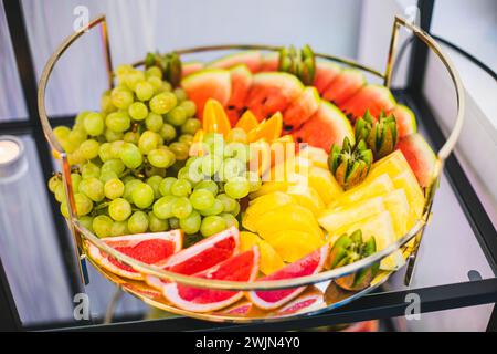 Round dish with variety of fresh fruits on buffet table at festive event. Mini snacks and treats.  Stock Photo