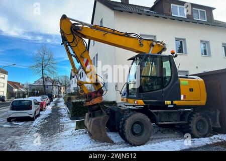 A yellow wheeled excavator standing in front of a residential building. Stock Photo