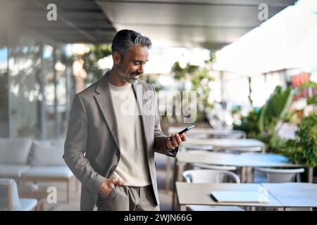 Happy middle aged business man standing in outdoor cafe using smartphone. Stock Photo