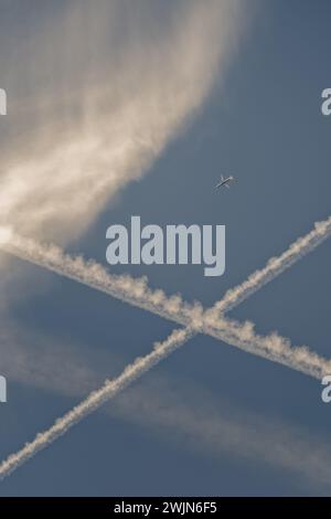 DIstant aeroplane/airplane in blue sky, with whispy cloud and crossed contrails. Stock Photo