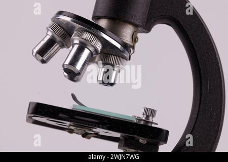 an old microscope stands on a white surface with real shadows, close up Stock Photo