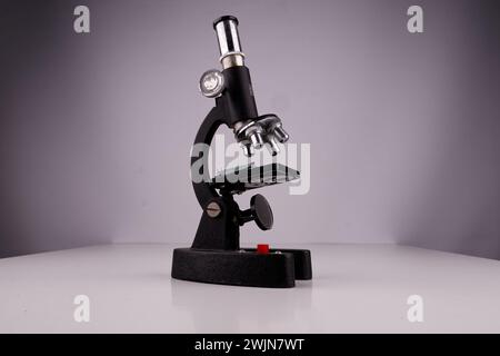 an old microscope stands on a white surface with real shadows, close up Stock Photo
