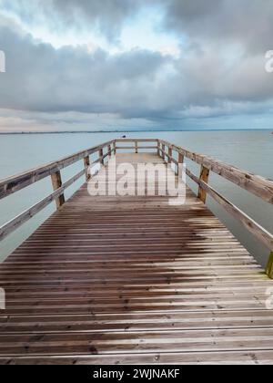 Empty wooden pier to the Ria de Aveiro in Portugal, with dramatic sky and calm water. Torreira, Murtosa - Portugal. Stock Photo