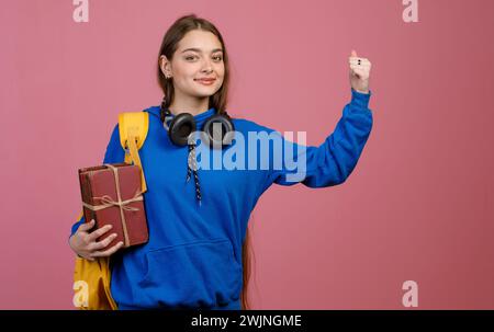 Brunette schoolgirl standing, raising hand, strong. Stock Photo