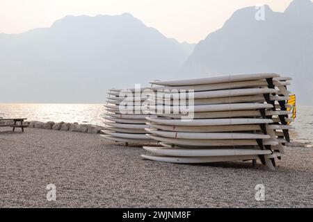 Stack up white paddle boards on a shore of lake Garda on a foggy day with mountains and trees in a bbackground. Italy lago di Garda Stock Photo